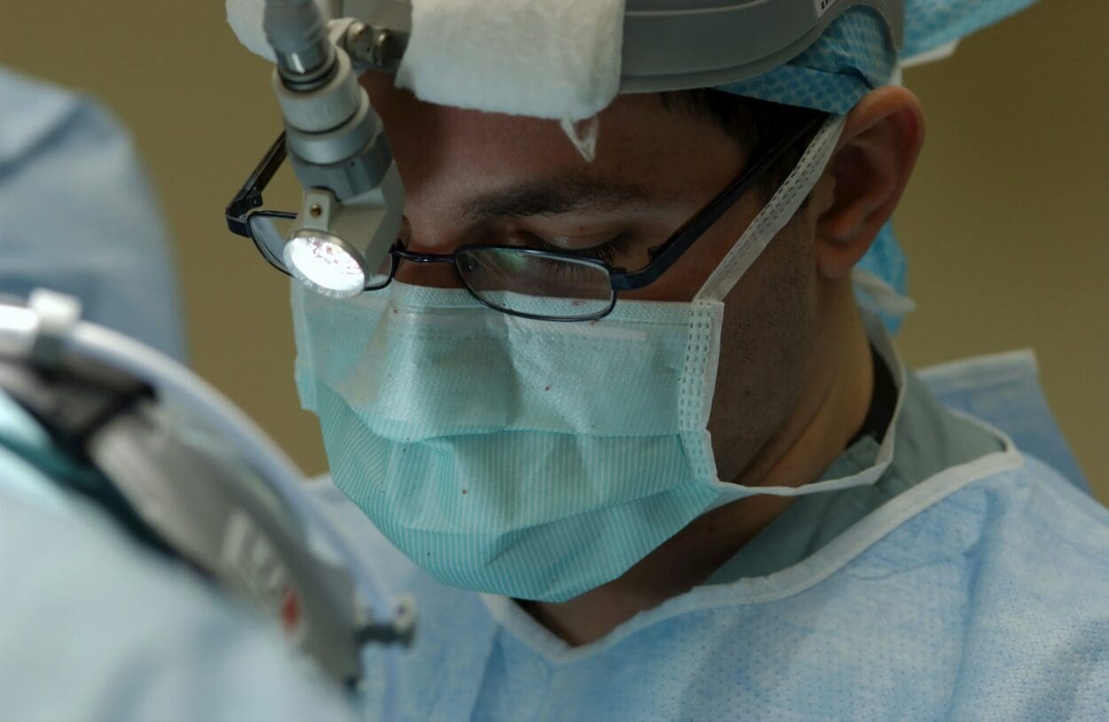 A focused medical student wearing surgical scrubs, a mask, and loupes during a procedure, embodying the theme of 'Empathy behind the Mask: Personal Stories of Grief from My Experience as a Medical Student.'