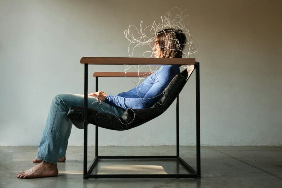 A person sitting in a chair with a tangled line illustration around their head, symbolizing the confusion and intense emotions experienced during the anger stage of grief.