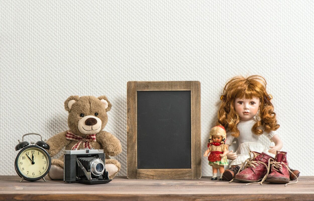 A nostalgic collection of childhood items including a teddy bear, dolls, an old camera, an alarm clock, and a pair of worn-out shoes, symbolizing the emotional attachment and grief often associated with letting go of personal possessions.