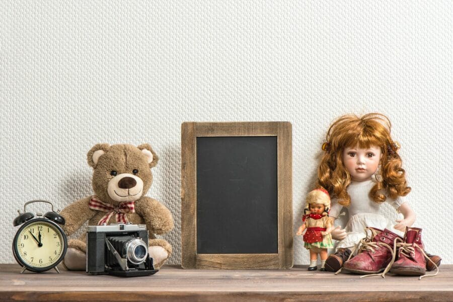 A nostalgic collection of childhood items including a teddy bear, dolls, an old camera, an alarm clock, and a pair of worn-out shoes, symbolizing the emotional attachment and grief often associated with letting go of personal possessions.