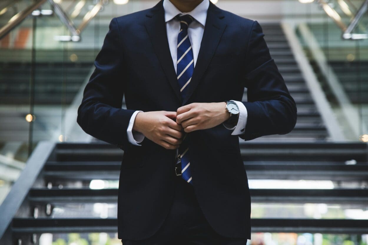 A person in a suit adjusting their jacket, standing on stairs, symbolizing the professional facade and the internal grief associated with job loss.