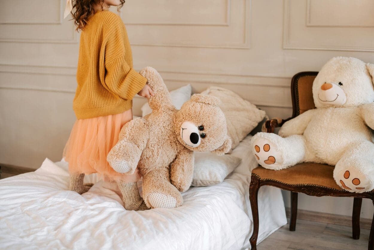 A child holding a large teddy bear on a bed, symbolizing comfort and support, reflecting the themes of guiding kids through loss and effective ways to support grieving children.