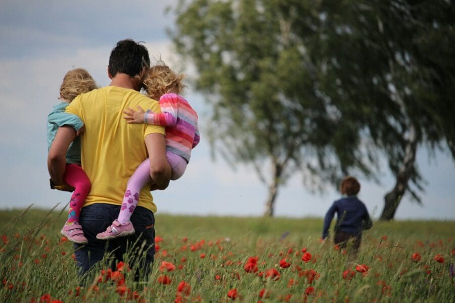 A father walking through a field of poppies, carrying two children while another child runs ahead, symbolizing the enduring bond and cherished memories shared with a father. This image resonates with quotes about the deep impact and lasting legacy of a father's love, even after his passing.