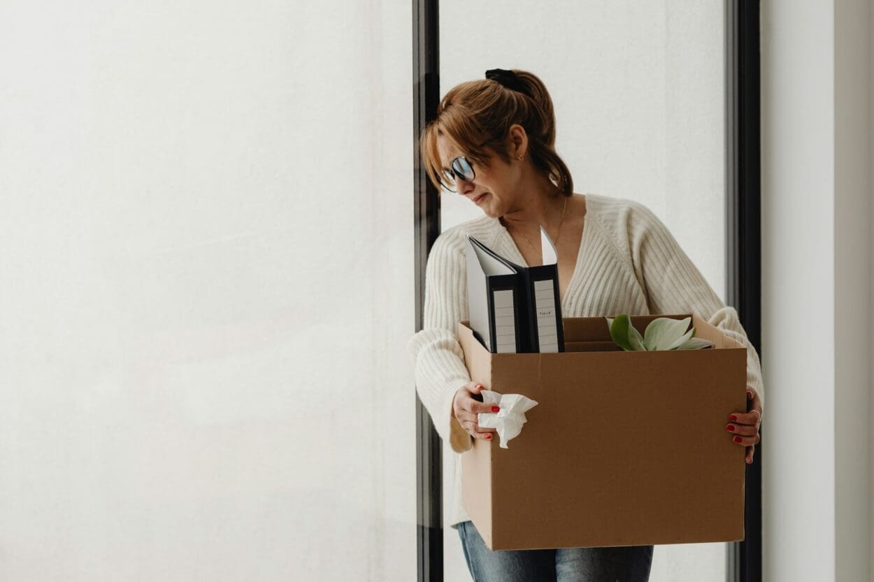 A woman carrying a box of personal belongings, symbolizing the emotional weight and grief associated with job loss.