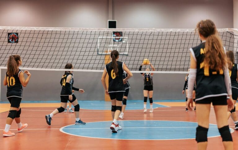 Young female volleyball players in black and yellow jerseys engaged in a game on an indoor court, with the net dividing the two teams. The atmosphere is focused and energetic, capturing the spirit of youth sports.