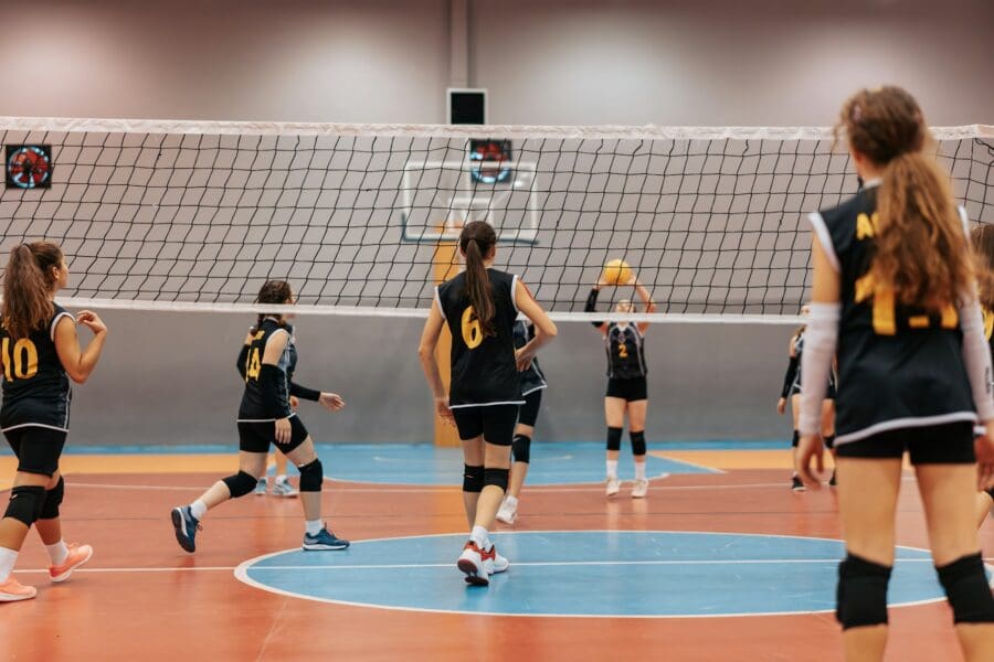 Young female volleyball players in black and yellow jerseys engaged in a game on an indoor court, with the net dividing the two teams. The atmosphere is focused and energetic, capturing the spirit of youth sports.