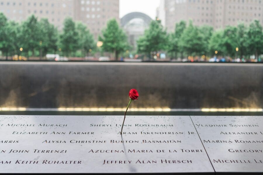 Close-up of a memorial with engraved names and a single red rose, symbolizing collective grieving and the shared remembrance of those lost.