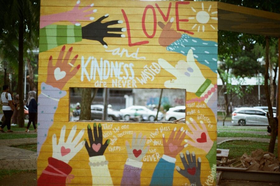 Colorful mural with outstretched painted hands and phrases about love and kindness, promoting compassion and support in a community setting.