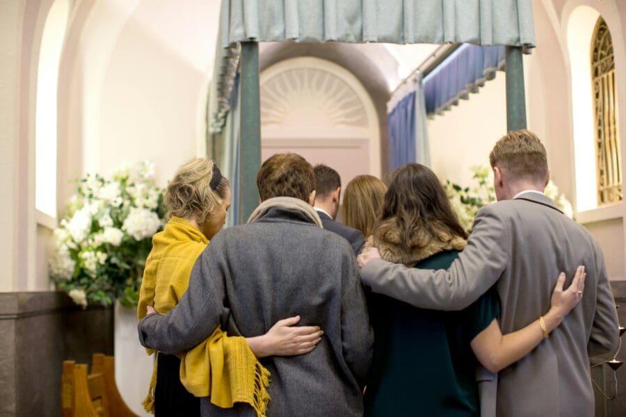 Family and friends gather closely together, offering support and comfort to each other during a funeral service. This image illustrates the role of funerals and memorial services in the grieving process, providing a space for collective mourning and honoring the memory of the deceased.