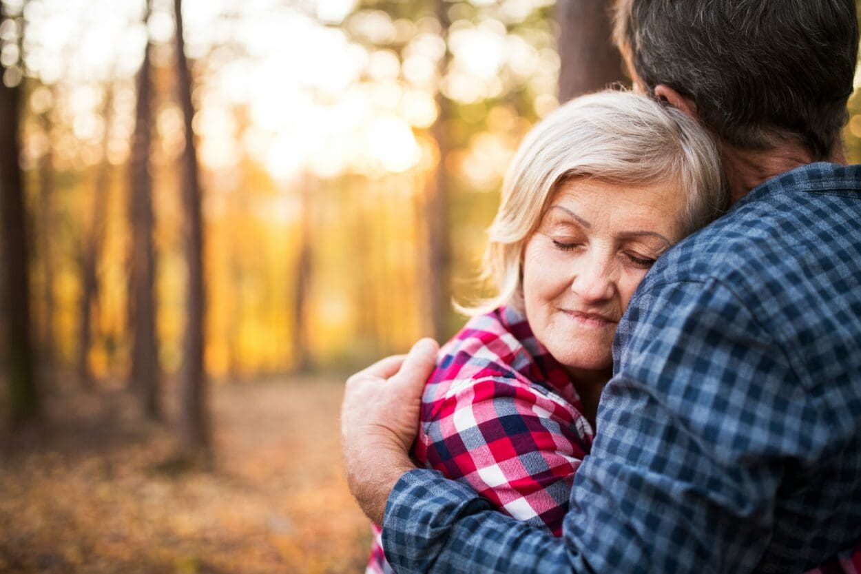 Senior couple embracing in a forest at sunset, symbolizing the rekindling of intimacy and connection after the loss of a spouse.