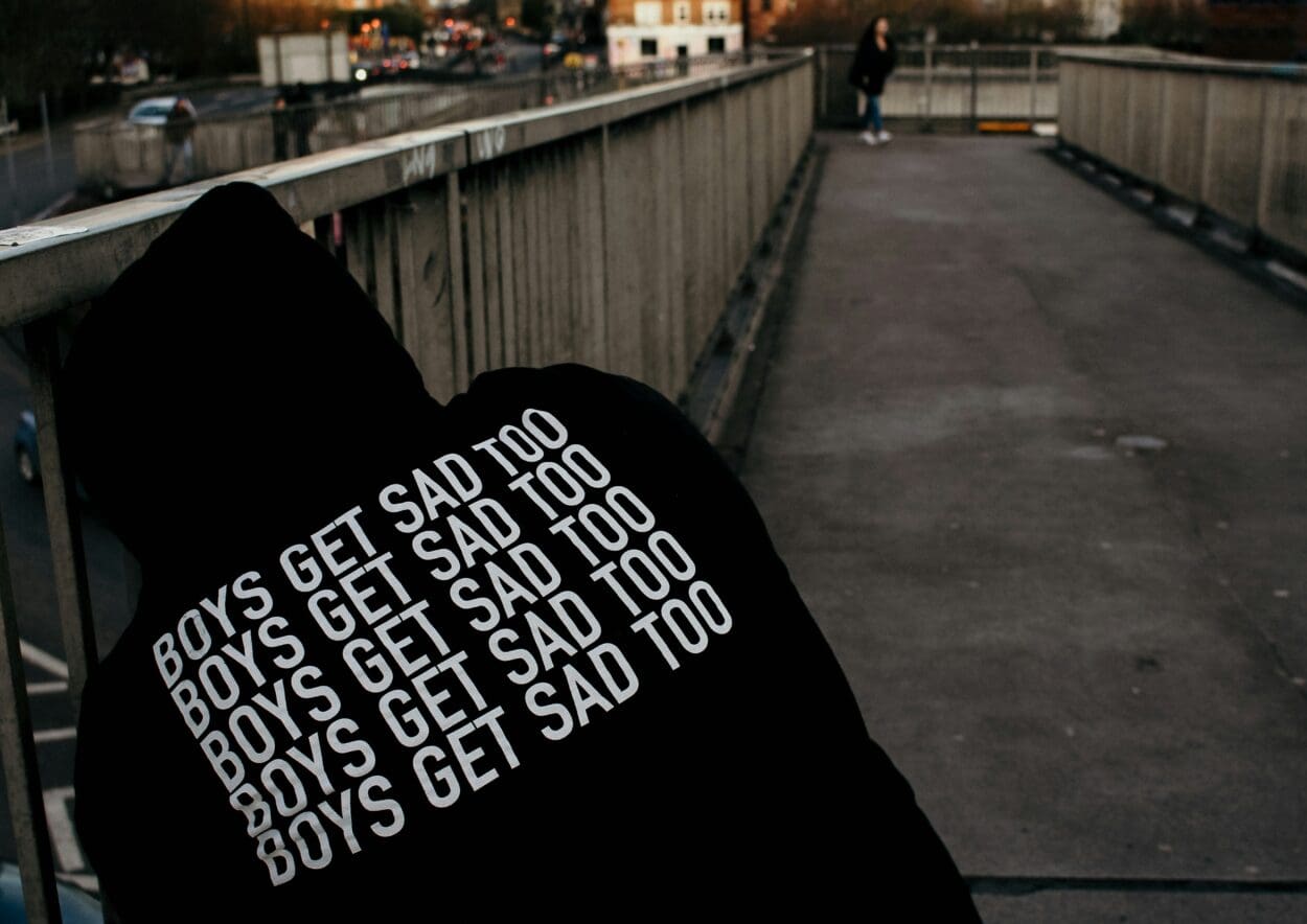 Male grief is real - pic of a male sitting with sweatshirt reading "boys get sad too"