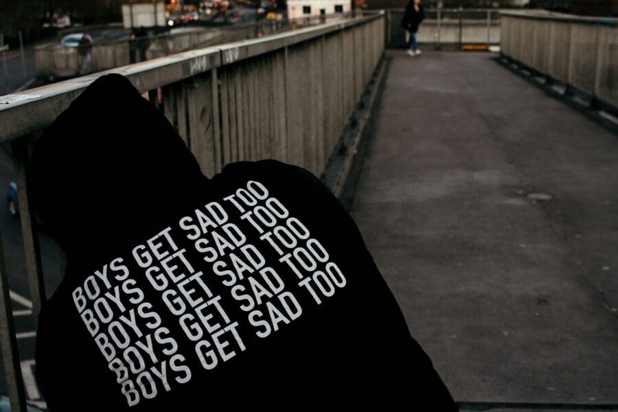 Male grief is real - pic of a male sitting with sweatshirt reading "boys get sad too"