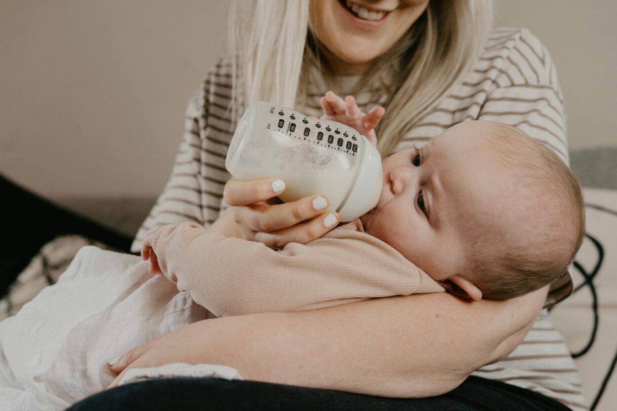 A smiling mother feeding her baby with a bottle, symbolizing the acceptance and emotional journey of mothers who transition from breastfeeding to bottle-feeding, embracing the 'fed is best' philosophy amid the redefinition of motherhood expectations.