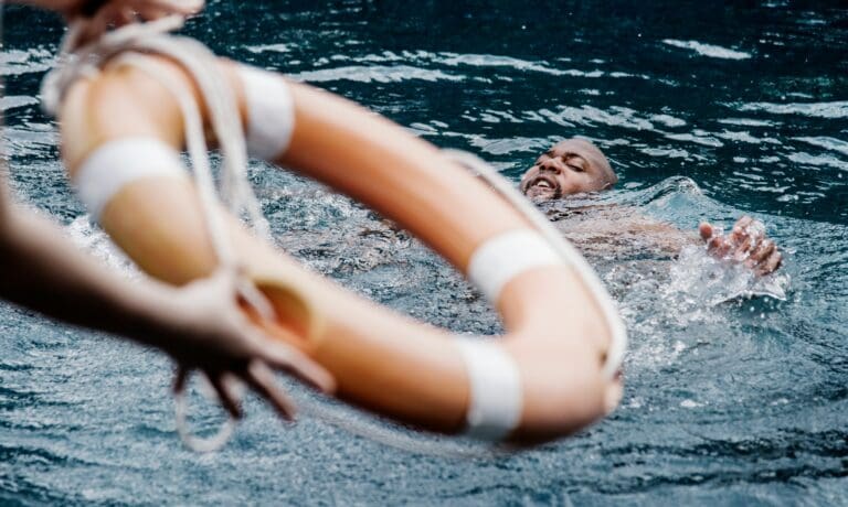 A man appearing to struggle in water as a lifebuoy is thrown towards him, symbolizing the overwhelming and suffocating sensations of grief, akin to the feeling of drowning.