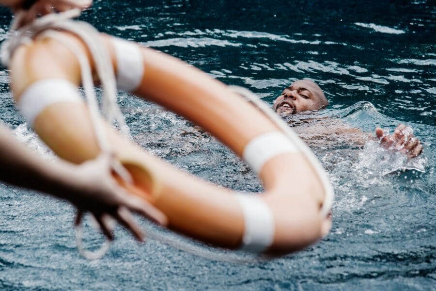 A man appearing to struggle in water as a lifebuoy is thrown towards him, symbolizing the overwhelming and suffocating sensations of grief, akin to the feeling of drowning.