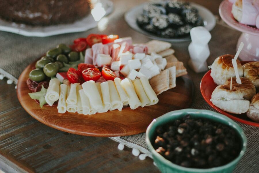 A comforting arrangement of cheeses, cold cuts, and tomatoes on a rustic wooden platter, illustrating how food is often used in grief rituals to provide comfort and bring people together during times of mourning.