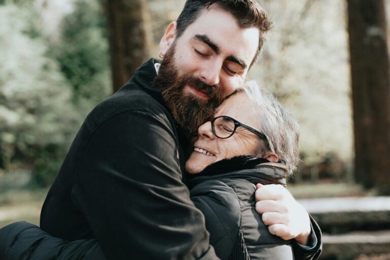 Heartwarming moment of a son embracing his elderly mother in a forest, reflecting love and support amidst the challenges of dealing with grief, loss and addiction.