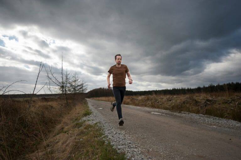 Man running along a gravel road in a remote area under a stormy sky, symbolizing the use of physical activity to cope with and process grief.