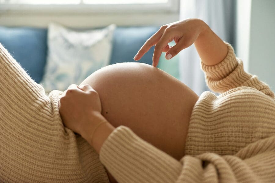 A pregnant woman gently touches her belly, contemplating her transformation into motherhood and the bittersweet emotions of leaving her past self behind as she embraces a new identity with hope and resilience.